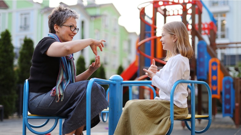 Adult woman and young girl conversing in sign language at a playground